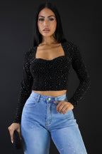 Woman wearing a black long-sleeve crop top with glitter and high-waisted blue jeans against a plain background