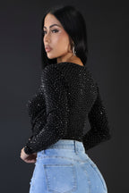 Woman wearing a black sequin top and light blue jeans against a plain background