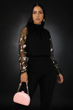 Woman wearing a black outfit with floral sheer sleeves against a white background