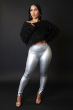 Woman wearing a black fuzzy sweater and silver leggings against a gray wall.