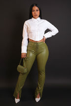 Woman wearing a white blouse and green pants holding a green handbag against a beige background