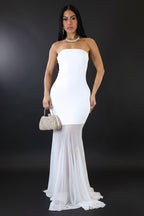 Woman wearing a strapless white dress with a sheer overlay on a plain background