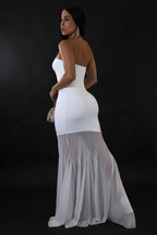 Woman wearing a white strapless gown with sheer overlay on a plain background