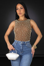 Woman wearing a sheer top with bead details and high-waisted jeans on a gray background