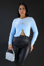 Woman wearing a light blue sweater and black pants holding a matching handbag against a plain background