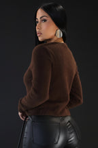 Woman wearing a brown sweater and black leather pants against a plain background