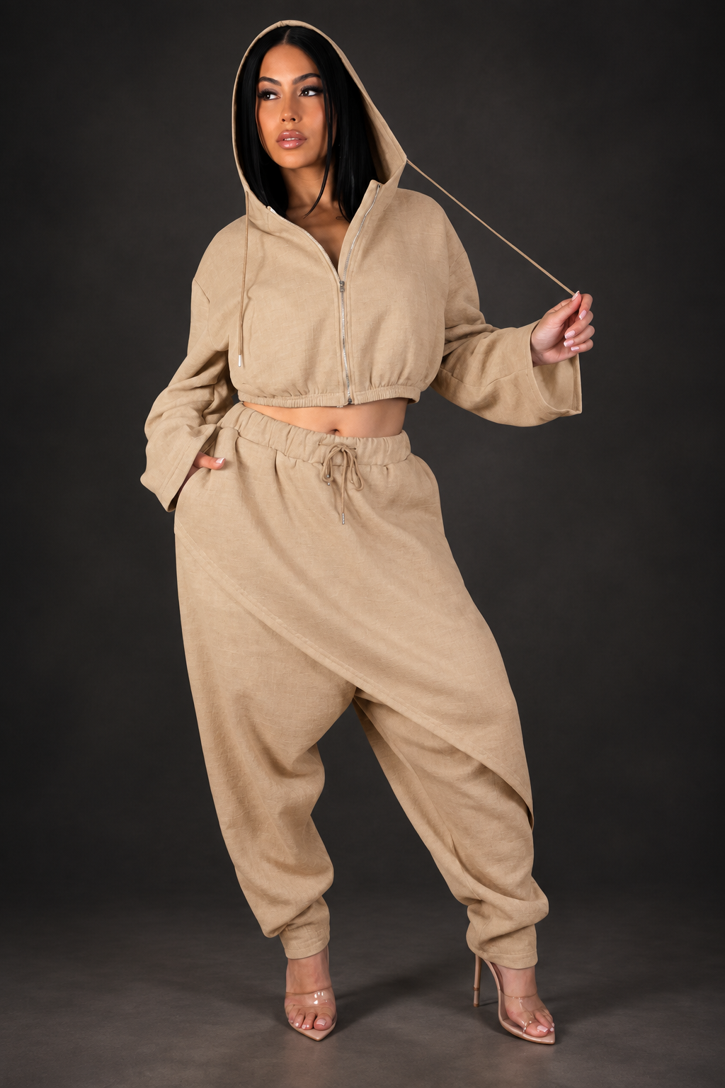 Model in tan pant set against a dark studio background